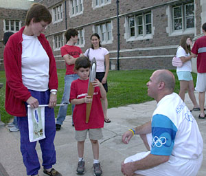 Six-year-old Jaelithe Downey examines one of the torches used in the relay, as Joan Downey, M.D., assistant professor of pediatrics in the Washington University School of Medicine, and torchbearer Rick Muhr look on.