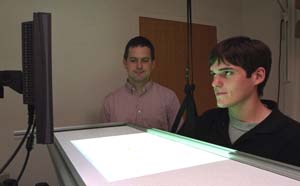 Kurt A. Thoroughman, Ph.D. (background), observes graduate student Jordan A. Taylor play a video game in the laboratory. Thoroughman and Taylor have tested human subjects and determined that the richness of motor training determines not only what humans learn but also how they learn.