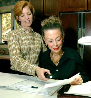 As part of the Occupational Therapy In-home and Community Home Services program, occupational therapist Monica Perlmutter (left) checks the lighting at a work area of client Gay Hirsch, who has low vision. Perlmutter has added a floor light to help Hirsch see her paperwork.