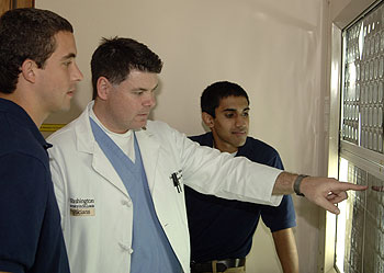 Greg Polites, M.D., assistant professor and assistant director of the Emergency Medicine Residency Program, shows Ian English (left) and Vikram Sasi, both pre-med students, a head CT scan demonstrating a brain injury and discusses the severity of the injury and the necessary treatment during a shadowing session for the Med Prep program.