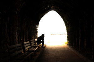 A depressed man next to a light in a tunnel.