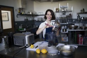 Deborah Gorman, in a blue apron, pours contents from a mixing bowl into a blender to make her Sorbabes vegan sorbet.