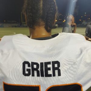 woman in sports uniform stands facing away from the camera in a white football jersey