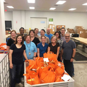 13 people stand for a group photo behind a cart full of orange bags