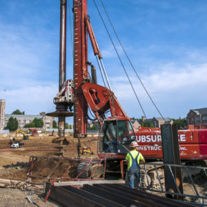 a man in a hard hat stands in front of a red construction vehicle in the middle of a work zone