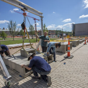 Two men install sculpture outside