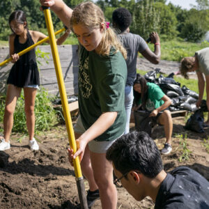 First-Year student shovels dirt into bag in a garden.