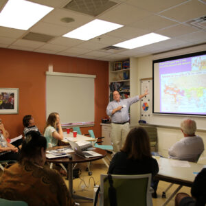 Man stands by a screen in front of a classroom filled with students.