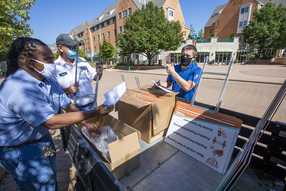 (From left) Yondell Bass and Rick Keune, both mechanics in maintenance, and Drew Thompson, a zone manager, install “Because” signage, part of WashU’s health and safety campaign, on the South 40. (Photo: Joe Angeles/Washington University)