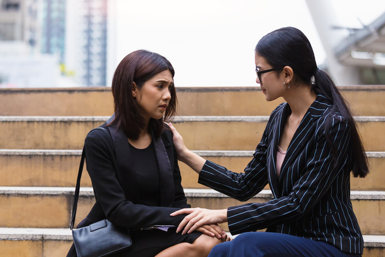 One woman offering support to another as they sit on steps outside