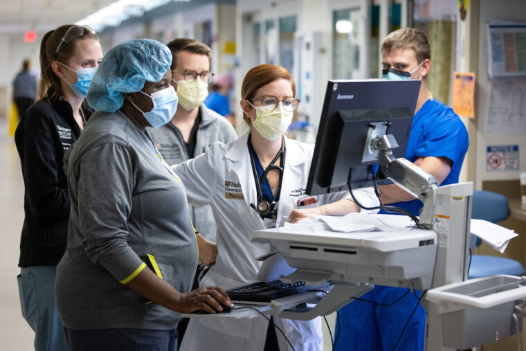 For nearly two years during the COVID-19 pandemic, doctors, nurses and other medical staff have taken care of patients in the intensive care unit at Barnes-Jewish Hospital. Here, nurse practitioner Marsha Johnson (blue cap); attending Rachel McDonald, MD (glasses); and other members of the care team confer outside a patient room on Nov. 5, 2020. (Matt Miller/Washington University School of Medicine)