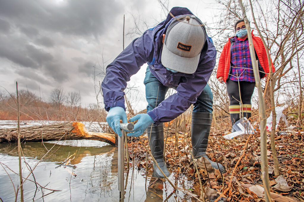 Rajesh Singh (left) is a research scientist in the Bose laboratory. Here, he collects a sample of soil along the shoreline at Ellis Island. Washington University biologists are searching for beneficial microbes in the wetlands. (Photo: Joe Angeles/Washington University)