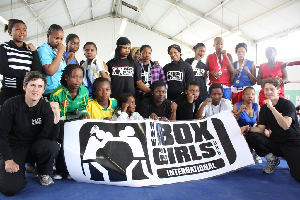 A group of girls wearing BoxGirls tshirts strike boxing poses in a white gym