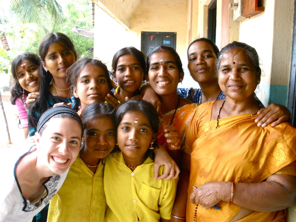 A group of Indian girls in brightly colored shirts pose and smile for the camera