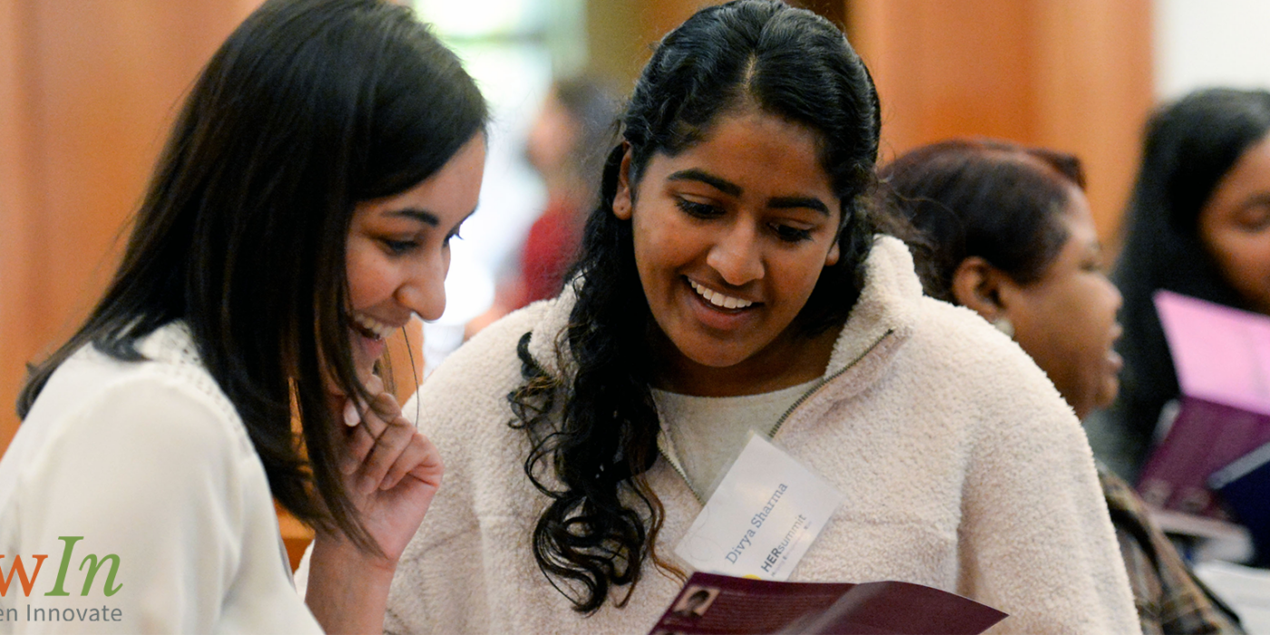 Two young women smile as they look at a brochure together