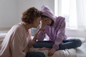 Image of worried mom comforting depressed crying teen daughter at home.