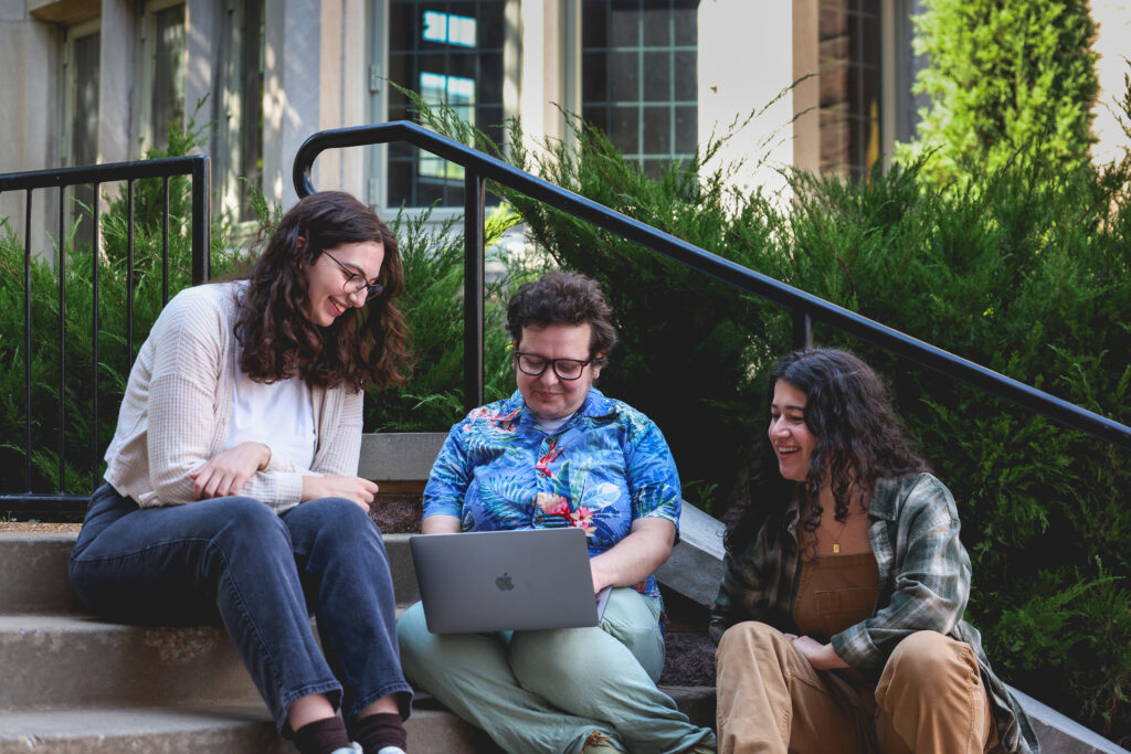 Three playwrights sitting on stoop and looking at laptop computer.