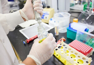 Lab tech holds a pipette over a glass bottle in a lab setting