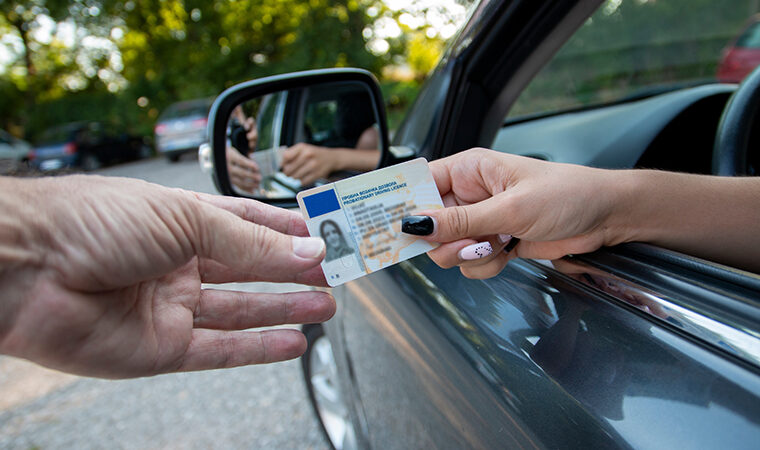 A picture of a young driver's hand giving license to a police officer through car window.