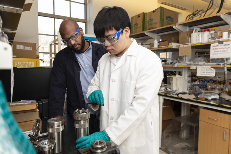 Marcus Foston looks over the shoulder of a student using equipment in a lab.