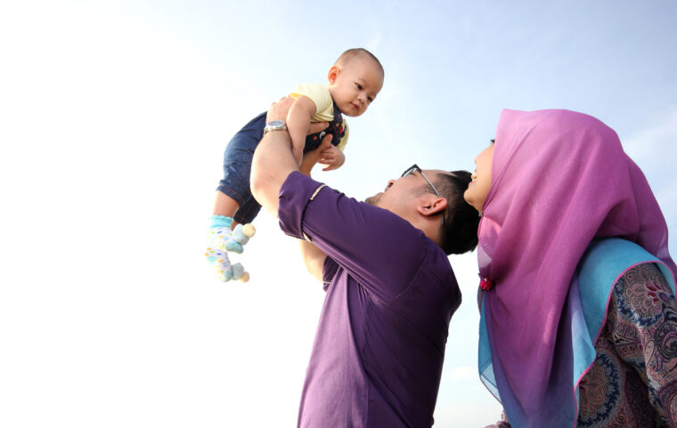 a happy father holds his baby while the mother looks on, smiling