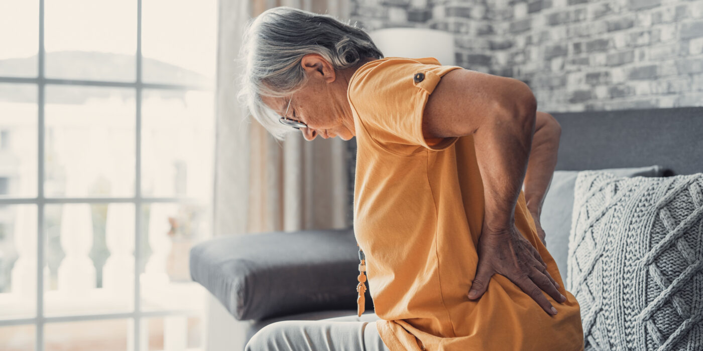 An elderly woman holds her lower back in pain