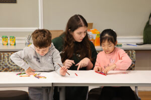 children coloring while a college student helps