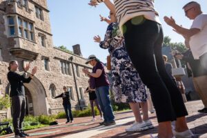 A group of people standing on a brick plaza hold hands up as a they do mindfulness movement at a university public space