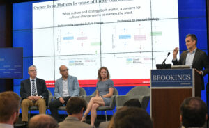 Seated panel of Bart Hamilton, Mike Mazzeo and Lynn Gorguze with Peter Boumgarden speaking at the commission presentation at the Brookings Institution.