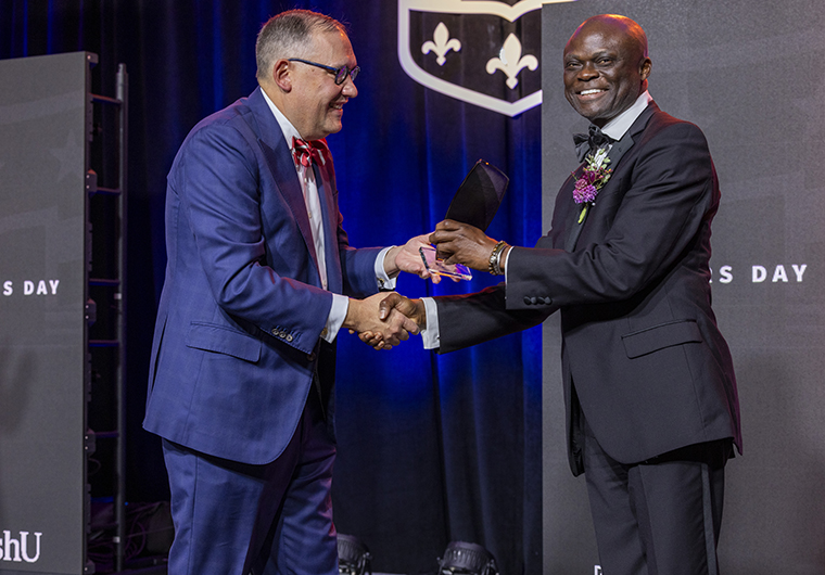 Chancellor Andrew Martin presents award to Fred M. Ssewamala on stage at Founders Day event.