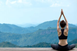 Woman in exercise clothing sits in a yoga pose overlooking forested hills