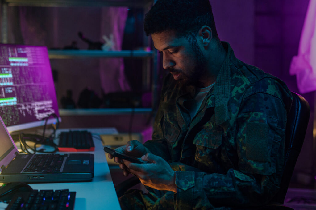 A soldier is looking at a phone in a dark office, representing army intelligence