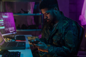 A soldier is looking at a phone in a dark office, representing army intelligence