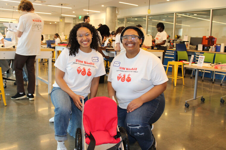 two young women in front of a small red wheelchair