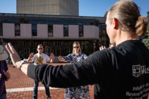a group of people doing gentle exercises lifting arms in a brick plaza