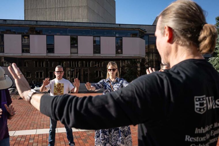 a group of people doing gentle exercises lifting arms in a brick plaza