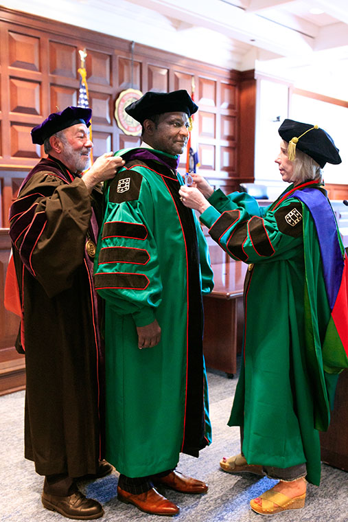 Stefanie Lindquist, the Nickerson Dean and professor of law at WashU Law, helps place the purple hood, signifying a degree in jurisprudence, over the Hon. Judge Edward Washington II at the ceremony on May 11. Washington’s former contracts professor Michael M. Greenfield, the George Alexander Madill Professor of Contracts & Commercial Law Emeritus, assisted Dean Lindquist.
