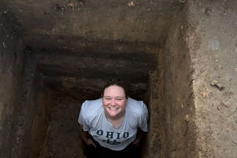 a woman smiling from a hole in the ground looking at layers of human civilization