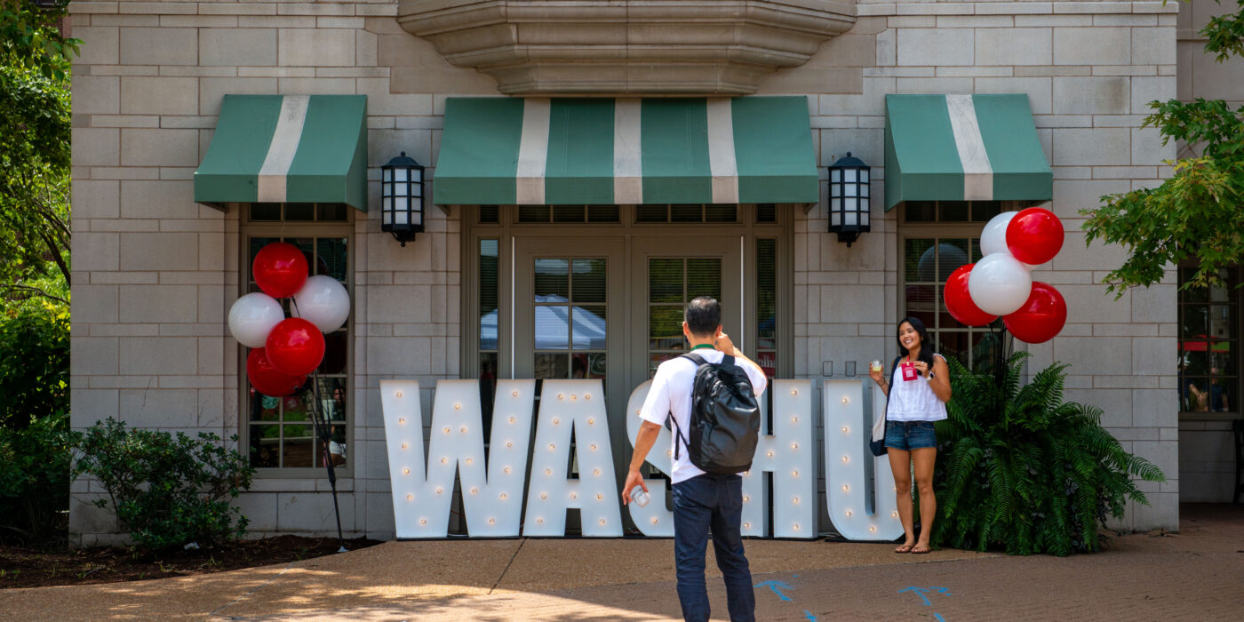 A student stands by a large WashU sign on move in day for the class of 2030