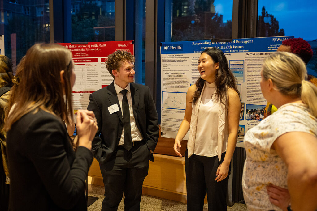 Two students in business attire stand before their posters and tell community members about their summer internships as St. Louis Fellows.