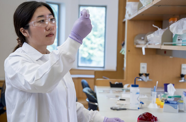 student in a lab coat holding up a sample