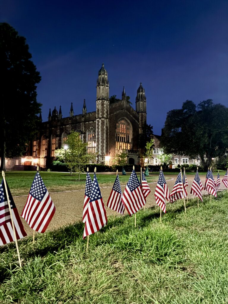 Small American flags line a field with Graham Chapel illuminated in the background.